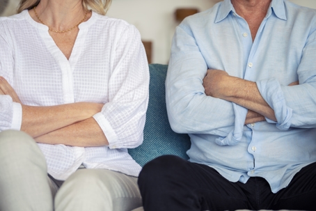 A divorcing couple sitting next to each other with their arms crossed.