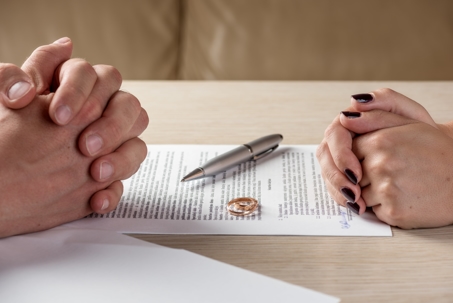 A cropped shot of a couple sitting across from another with divorce decree and wedding rings between them, hands clasped.